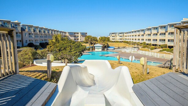 A view of a resort with a pool, a slide, and multi-story buildings. - A Place at the Beach - 2 bedroom, 2 baths - Pools, Waterslide, Mini-golf & more! (Atlantic Beach)