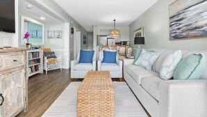 A living room with a white sofa, two armchairs, a coffee table, and a bookshelf. - A Place at the Beach - 2 bedroom, 2 baths - Pools, Waterslide, Mini-golf & more! (Atlantic Beach)