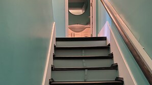 Eine Treppe mit Holzdielen und weißen Geländern, die zu einem Raum mit einem runden Spiegel und einem Waschbecken führt.