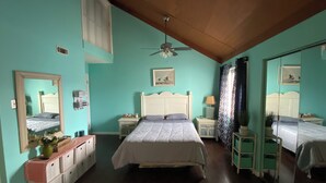 Ein Schlafzimmer mit einem Bett, Nachttischen, einem Spiegel und einem Deckenventilator.
