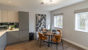 Een moderne keuken met grijze kastjes, een eettafel voor vier personen en een groot abstract schilderij aan de muur.