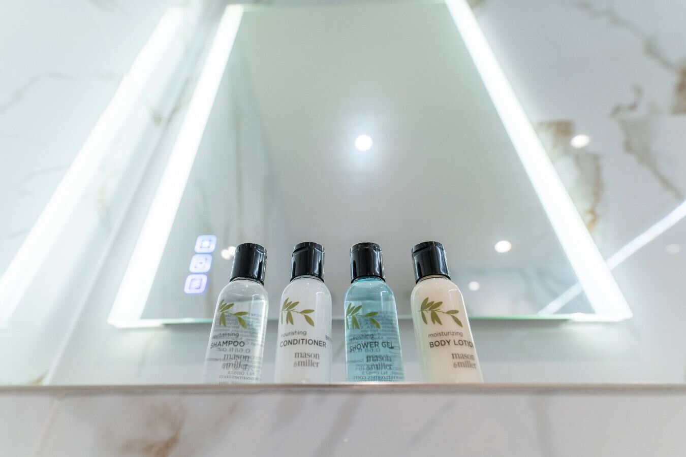 A bathroom with a mirror and four bottles of toiletries on the counter.