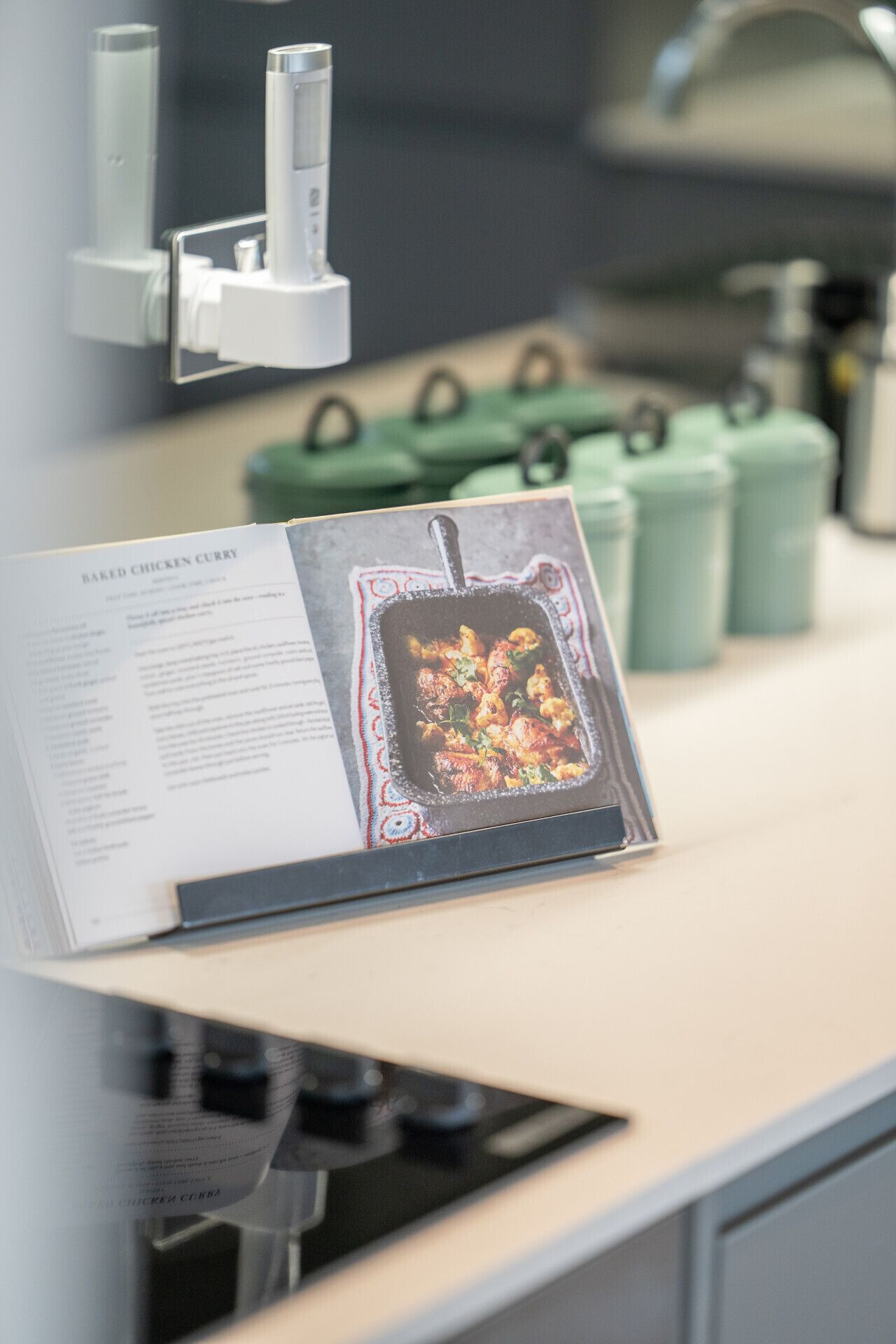 Un livre de recettes ouvert sur un plan de travail de cuisine, avec une cuisinière et des récipients verts en arrière-plan.