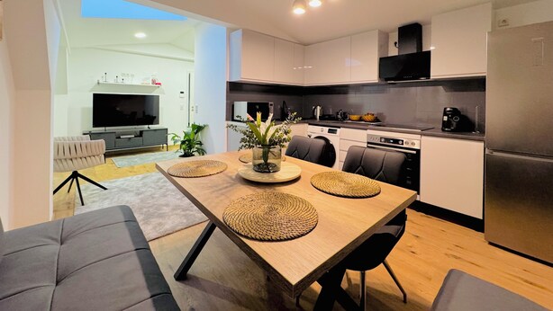 Een moderne keuken met een eethoek, met een houten tafel, stoelen en een televisie op de achtergrond.