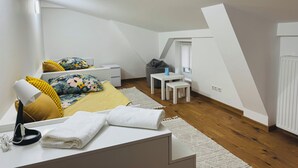 Een moderne, goed verlichte slaapkamer op zolder met een schuine kap, een bed met bloemenbeddels, een bureau, een stoel en een radiator.