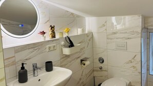 Een moderne badkamer met een wit wastafelmeubel, spiegel, toilet en marmeren tegels.