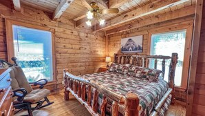 A log cabin bedroom with a wooden bed, a rocking chair, and a ceiling fan. - A Bear’s Eye View – Epic 4BR 3BA Cabin wGame Room, Hot Tub & Stunning Vistas!  (Sevierville)
