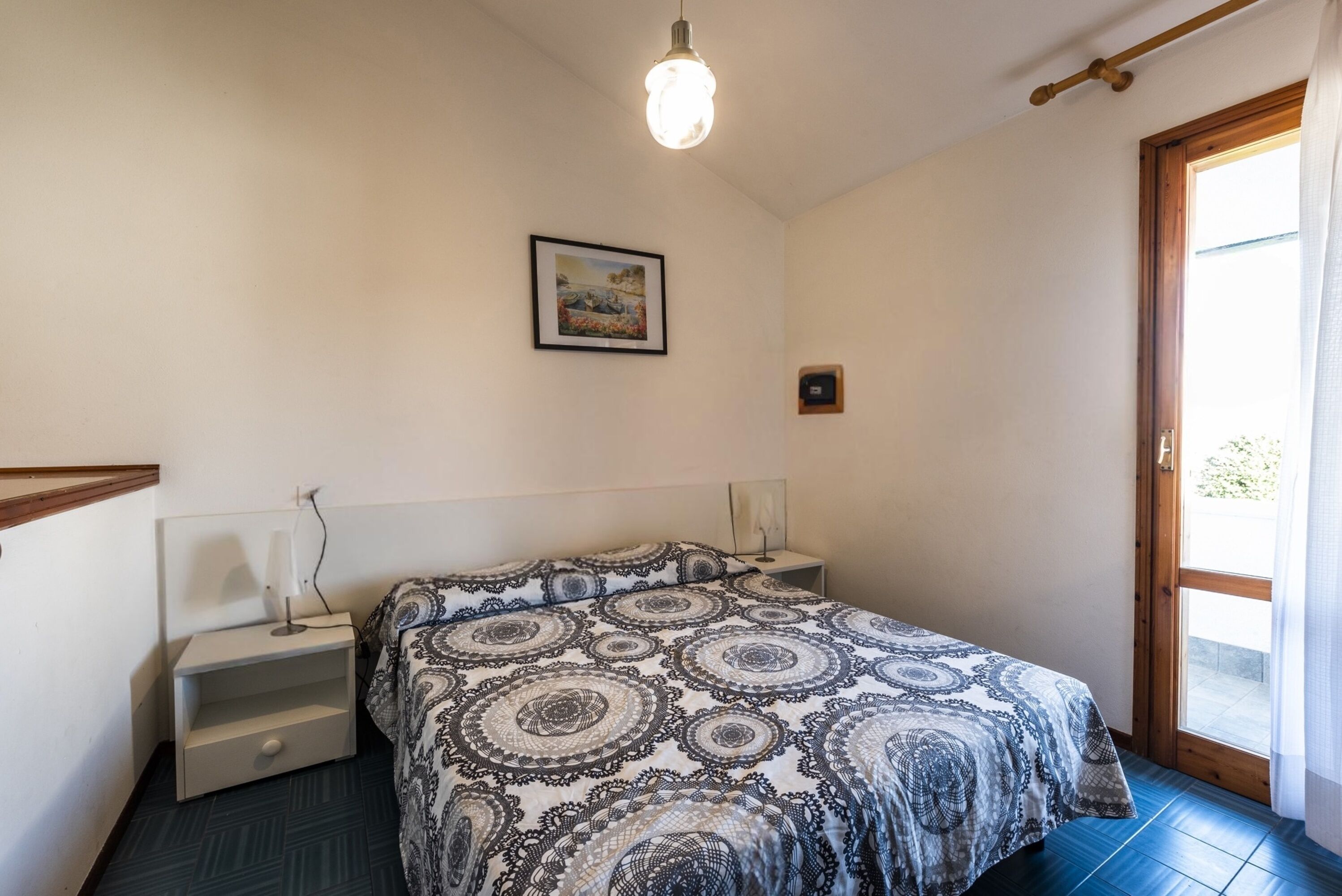 Un dormitorio con cama, mesitas de noche, un cuadro enmarcado en la pared y una ventana con vistas.