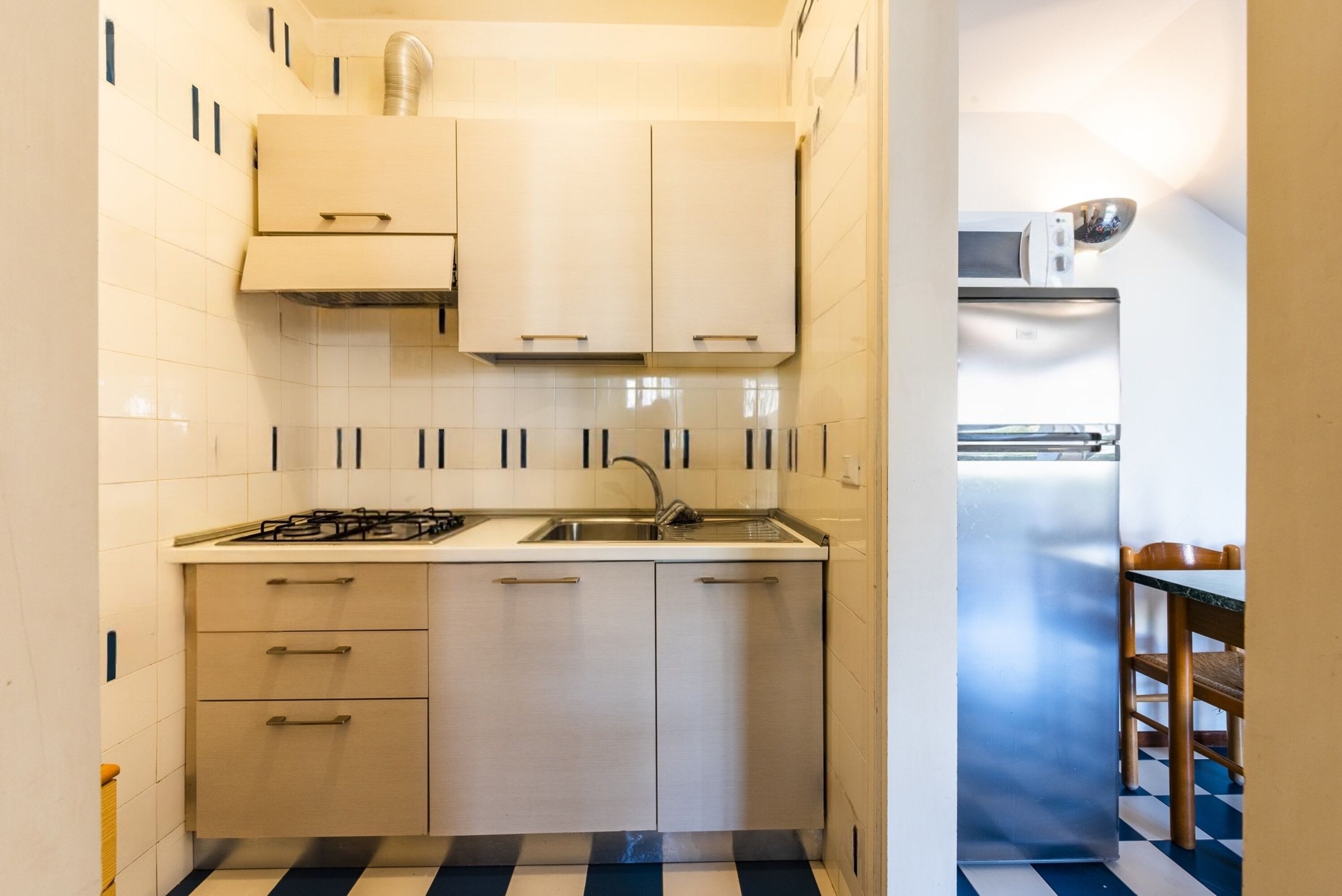 A compact kitchen with a gas stove, sink, and a stainless steel refrigerator.