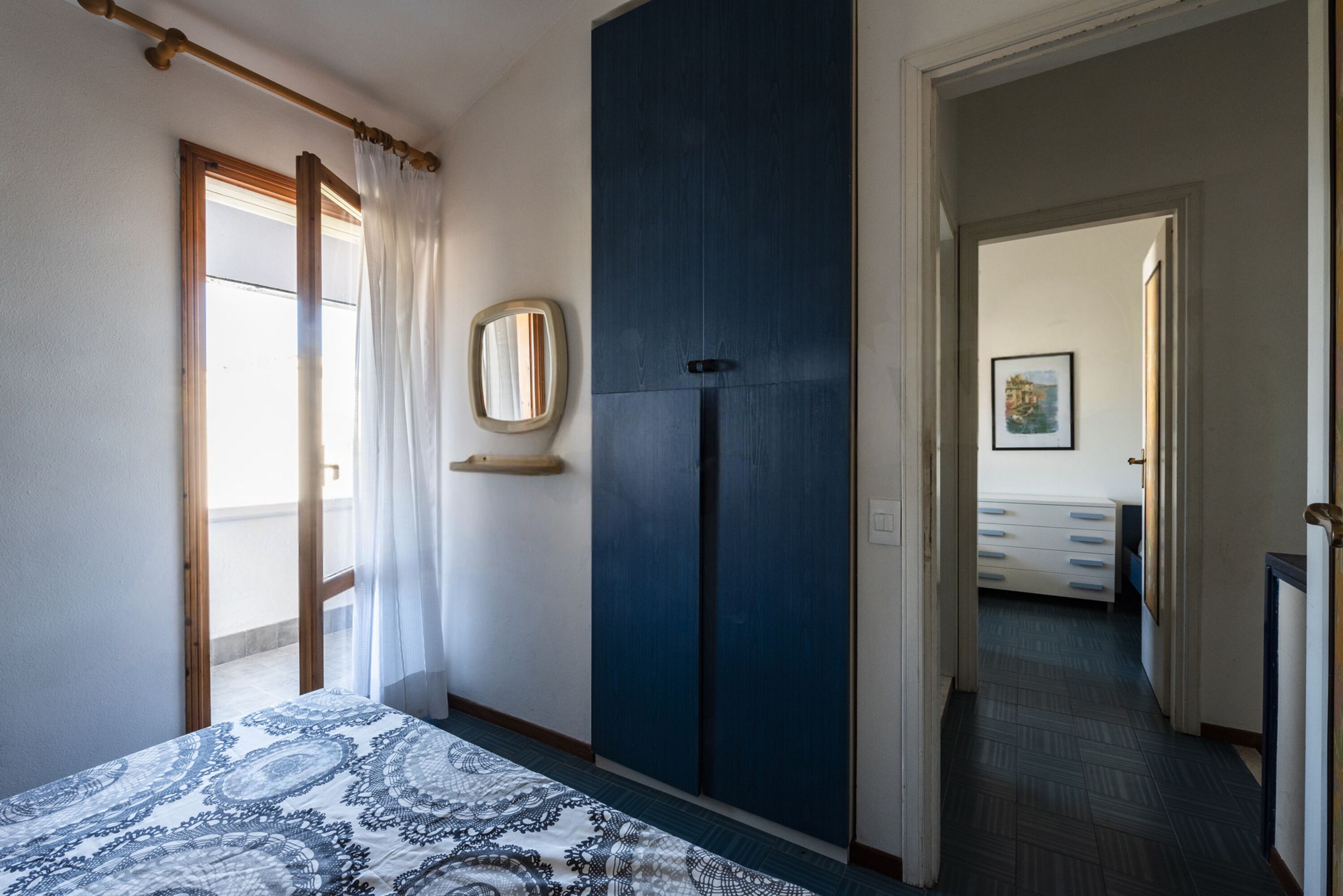 A bedroom with a bed, a wardrobe, a mirror, and a door leading to another room.