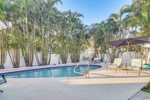 A swimming pool with a blue tiled edge, surrounded by palm trees and a white fence. There are two lounge chairs with a patterned cover and a metal pool ladder. - 2 Mi to Beach: Home w/ Pool, Grill & More in Largo (Largo)