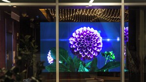 A modern interior with a large digital display of a purple flower, a glass partition, and a seating area with a small table. - Oasis 2BD/2BA near Beverly Grove w/ Parking, Gym and in unit Washer/Dryer (Los Angeles)