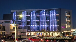 A modern building with illuminated facade, multiple floors, and a parking area with cars. - Oasis 2BD/2BA near Beverly Grove w/ Parking, Gym and in unit Washer/Dryer (Los Angeles)