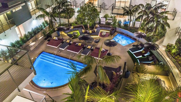 An indoor pool area with multiple seating areas, palm trees, and a large pool. - Oasis 2BD/2BA near Beverly Grove w/ Parking, Gym and in unit Washer/Dryer (Los Angeles)