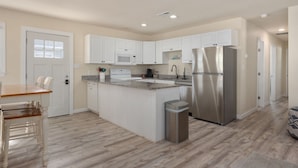 A modern kitchen with white cabinets, stainless steel appliances, and a wooden dining table. - Pool/Hot tub -Fenced yard -1 dog friendly (Nags Head)