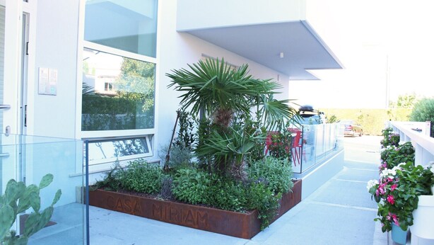 A modern building with large windows, a metal planter with greenery, and a clear view of the street. - Dainese Apartments, Casa Miriam (Jesolo)