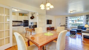 A modern kitchen with white cabinets, a dining table with chairs, a TV, and a living area with a sofa and lamp. - 4 Mi to FSU! Family Gem w/ Deck in Tallahassee (Tallahassee)