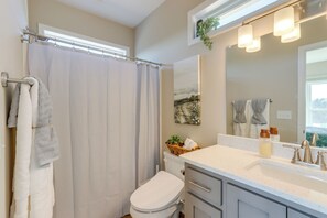 Een badkamer met douchegordijn, toilet, wastafel met spiegel en raam met plant.