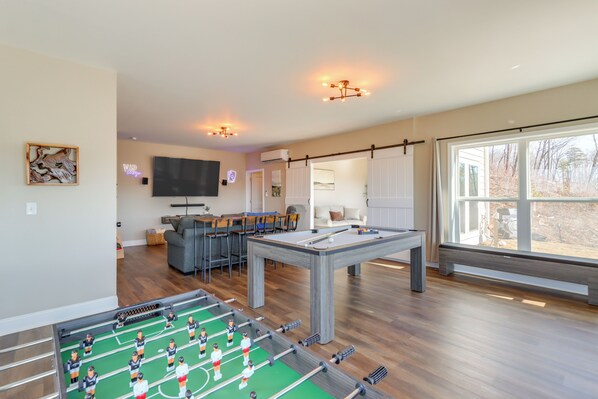 Een ruime woonkamer met een tafelvoetbal tafel, een pooltafel en een aan de muur bevestigde televisie.