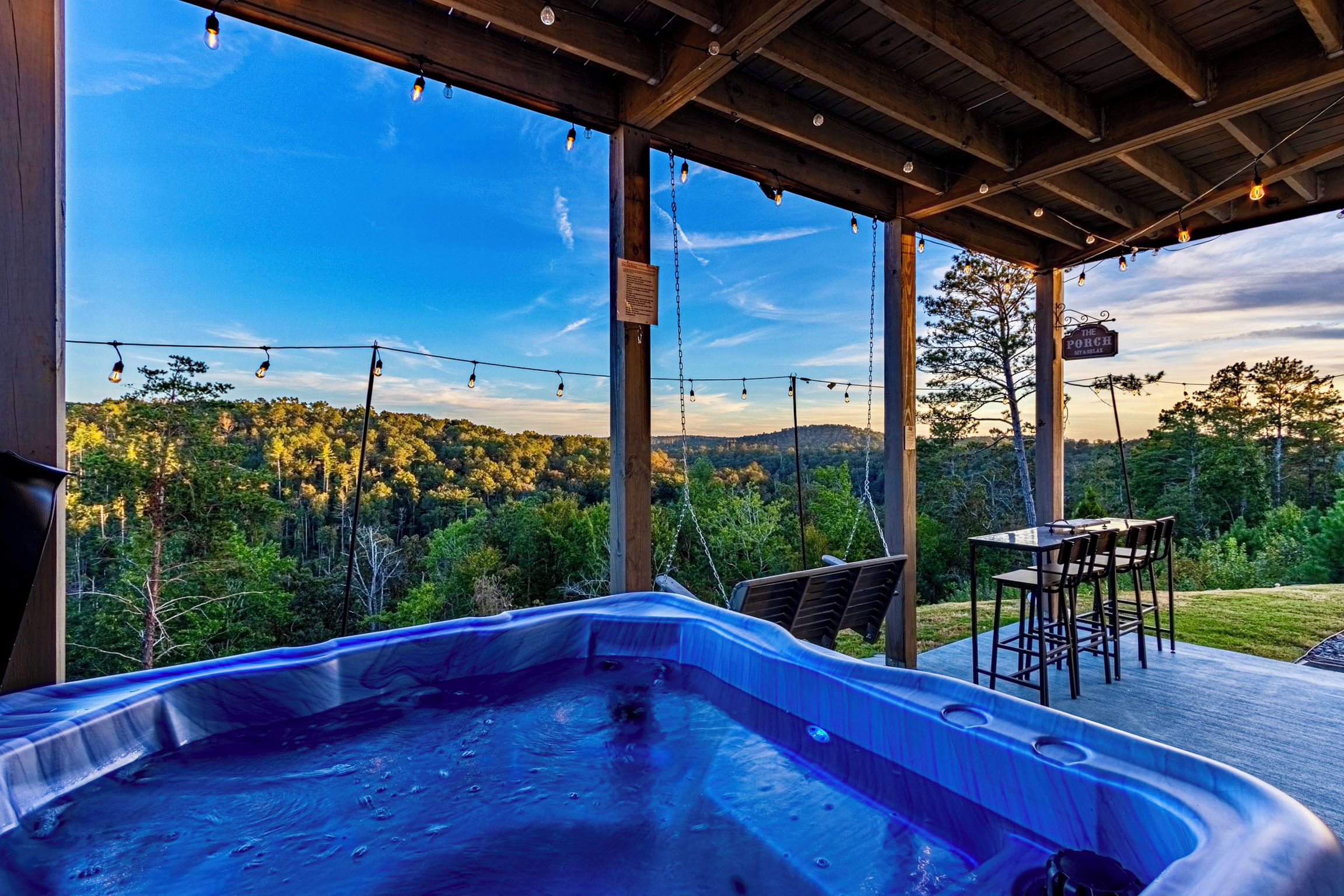 A hot tub under a wooden pergola with a view of a forested landscape.