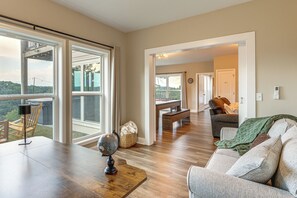 A spacious living area with a wooden floor, a sofa, a dining table, and a large window offering a view of the outdoors. - Luxury Cabin, Mountain Views, Hot Tub, EV Charger (Ellijay)