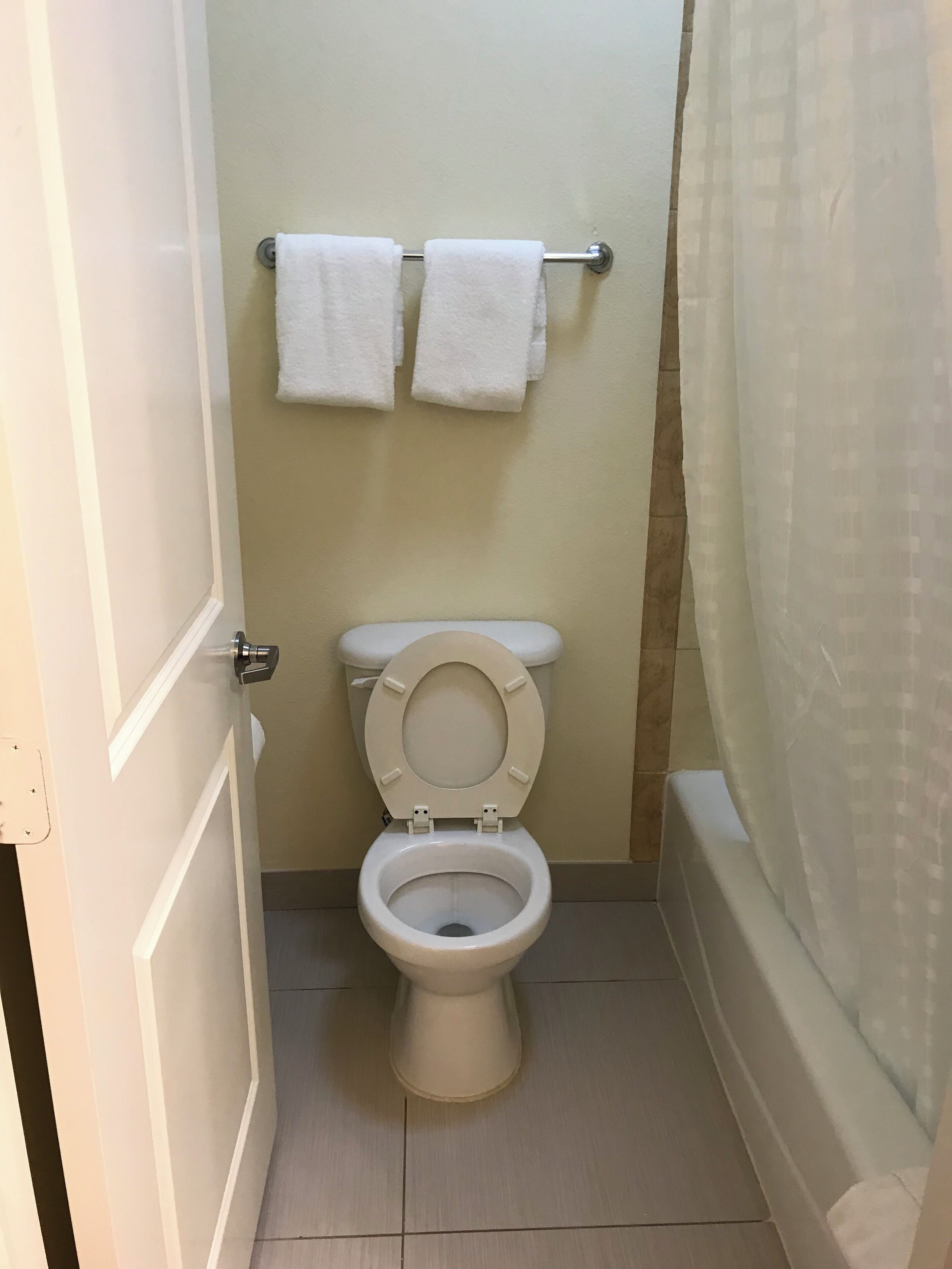 Un baño pequeño con inodoro, dos toallas en un escurridor y cortina de ducha.