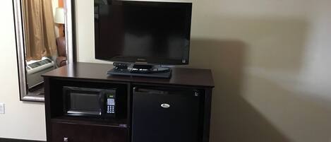 A hotel room with a flat-screen TV on a wooden dresser, a microwave, and a small refrigerator.
