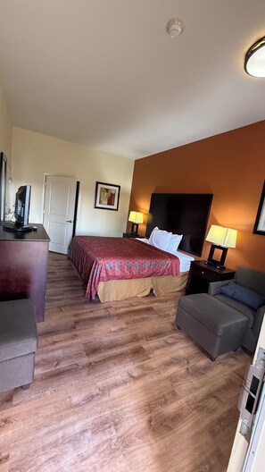 A hotel room with a bed, a desk, a chair, a sofa, and a TV.