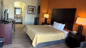 A hotel room with a bed, bedside tables, a desk, a chair, and a bathroom visible in the background. - Executive Inn & Suites (Pittsburg)