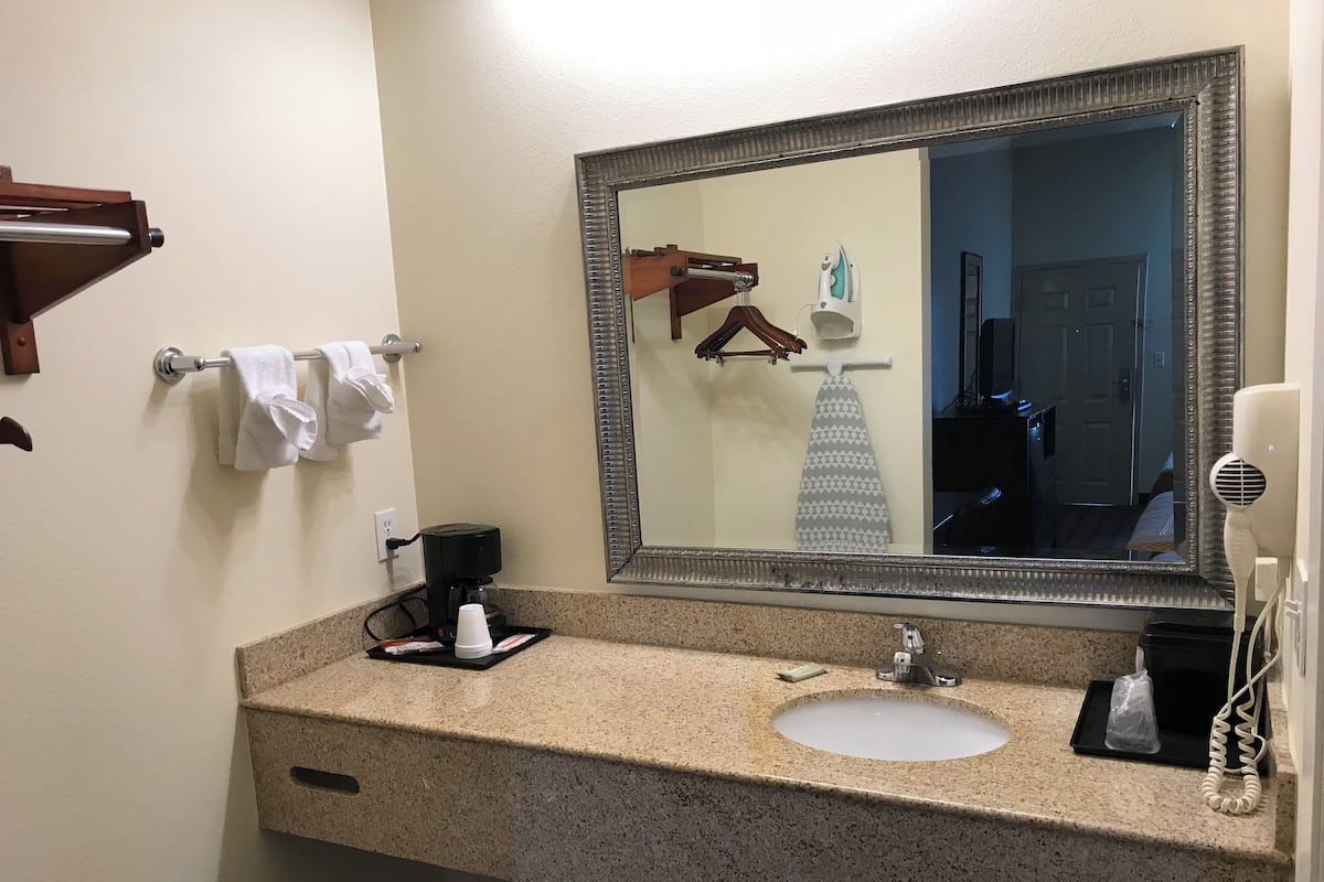 A hotel bathroom with a granite countertop sink, a mirror, a towel rack, a hairdryer, and a coffee maker.
