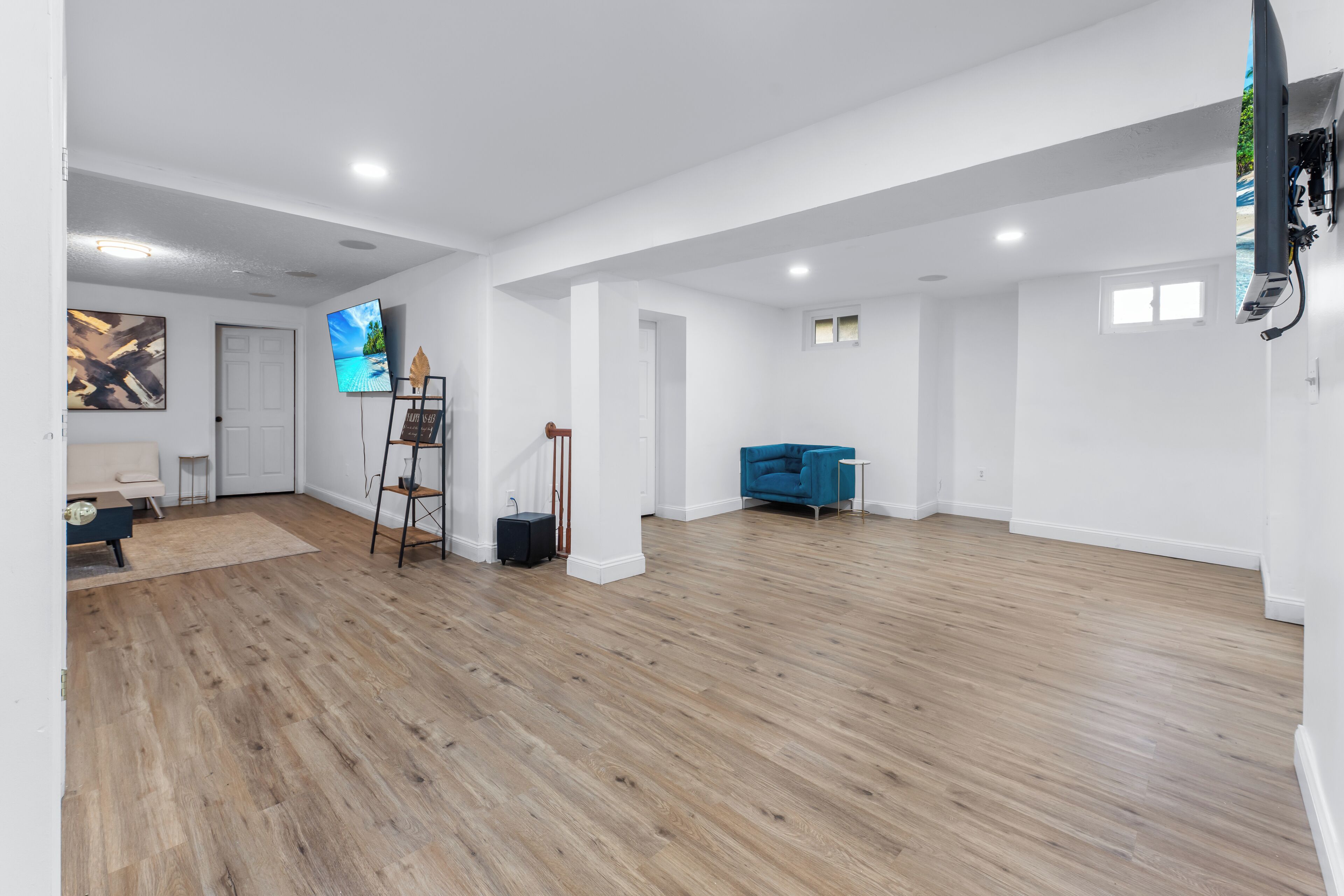 A spacious room with wooden flooring, a blue sofa, a TV mounted on the wall, and a ladder.