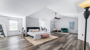 Un dormitorio amplio con una cama grande, un ventilador de techo y un sillón verde.
