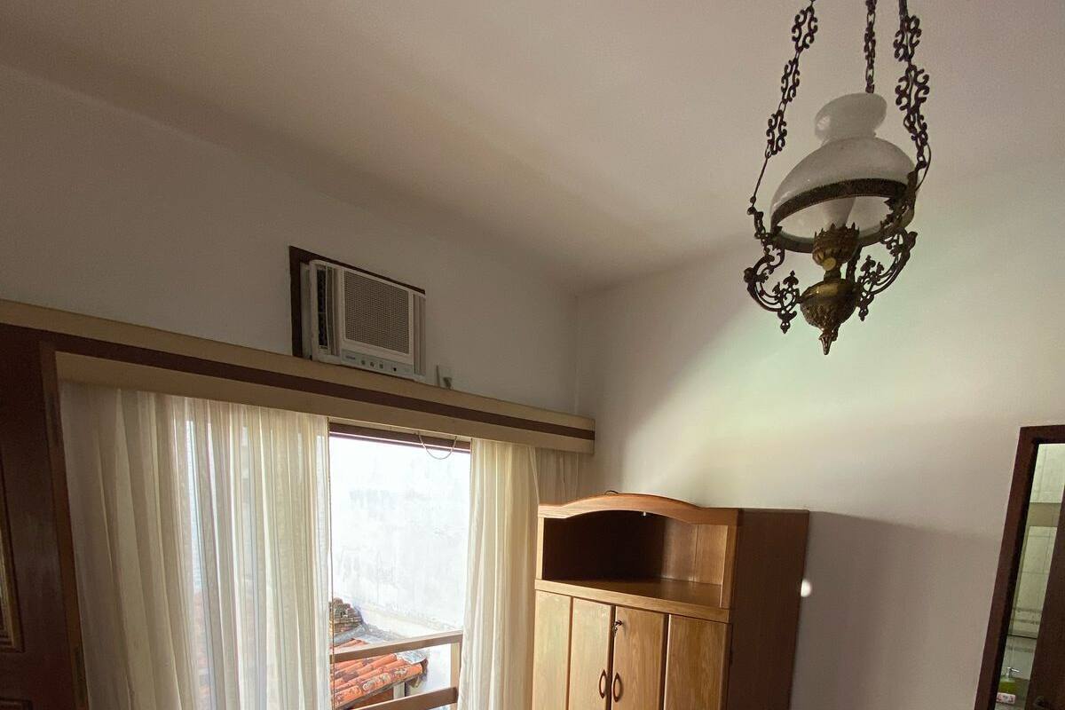 A room with wooden flooring, a wooden wardrobe, a pink bed with rolled-up towels, a chandelier, and a view through a window with curtains.