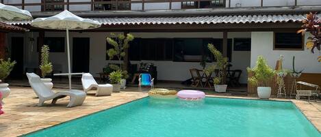 A swimming pool with lounge chairs and umbrellas, surrounded by a building with multiple windows and balconies.