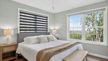 A bedroom with a bed, bedside lamps, a ceiling fan, a window with a view, and a bench.