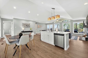 A modern kitchen with a central island, white cabinetry, and a dining area with a round table and chairs.