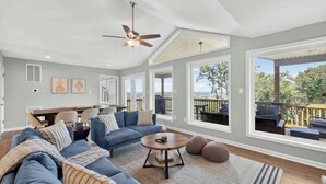 A spacious living room with a sectional sofa, a round coffee table, and large windows offering a view of the outdoors. - Mountain View Cottage | Hot Tub & Game Room (Front Royal)