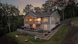 A two-story house with a balcony, a stone retaining wall, and a well-maintained lawn.
