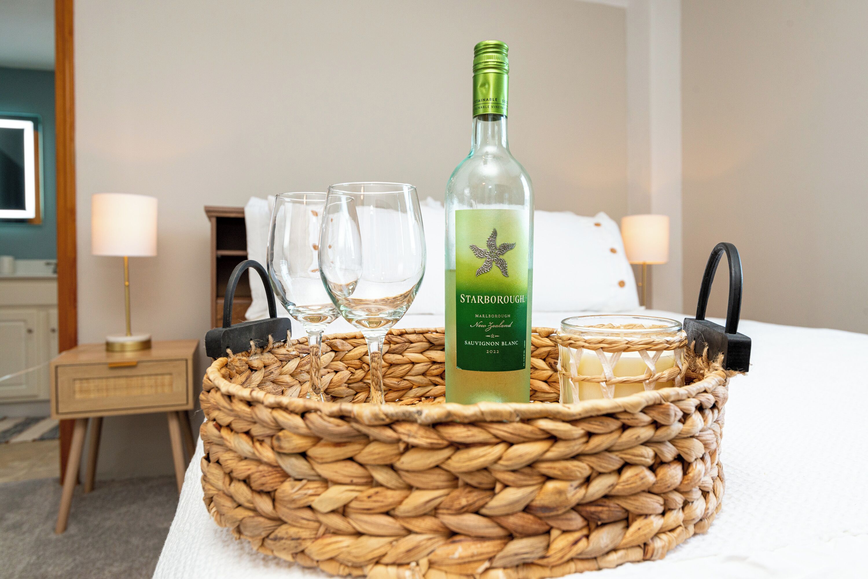 A wicker tray with a bottle of Starborough Sauvignon Blanc, two glasses, and a candle on a bed.