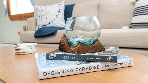 Un cuenco de vidrio sobre un soporte de madera con libros, incluyendo 'Shades of Grey' y 'Designing Paradise', sobre una mesa de madera.
