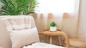 Un rincón acogedor con un sillón mullido, una mesita con planta en maceta y un taburete tejido.