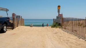 Entrada a la playa con una valla de madera, un cartel que indica acceso a la playa nivel 5 y un letrero de no estacionamiento.