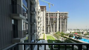 A modern building with balconies, a construction site in the background, and a pool area. - Magnificent 2 bedroom Golfville+ Pool View (Dubai)