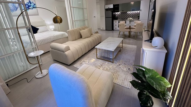 A modern living room with a sofa, coffee table, and a dining area with chairs. - Magnificent 2 bedroom Golfville+ Pool View (Dubai)