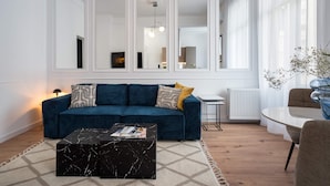 A modern living room with a blue sofa, a black marble coffee table, and a dining area with a glass table and chairs. - Elegant & Bright 2BR Condos - Steps from Old Town (Bucharest)