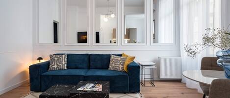 A modern living room with a blue sofa, a black marble coffee table, and a dining area with a glass table and chairs.