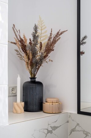A bathroom with a marble countertop, a black vase with dried plants, a white candle, and a mirror.