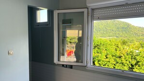 A room with a bed, a window with a view of greenery, and a ceiling light. - Alamanda pink (Sainte-Anne)