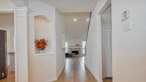 A spacious hallway with a wooden floor, white walls, and a small flower arrangement on the left.