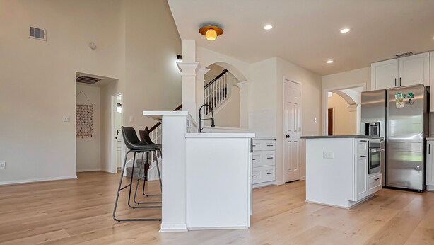 A spacious kitchen with white cabinetry, a stainless steel refrigerator, and a wooden floor.